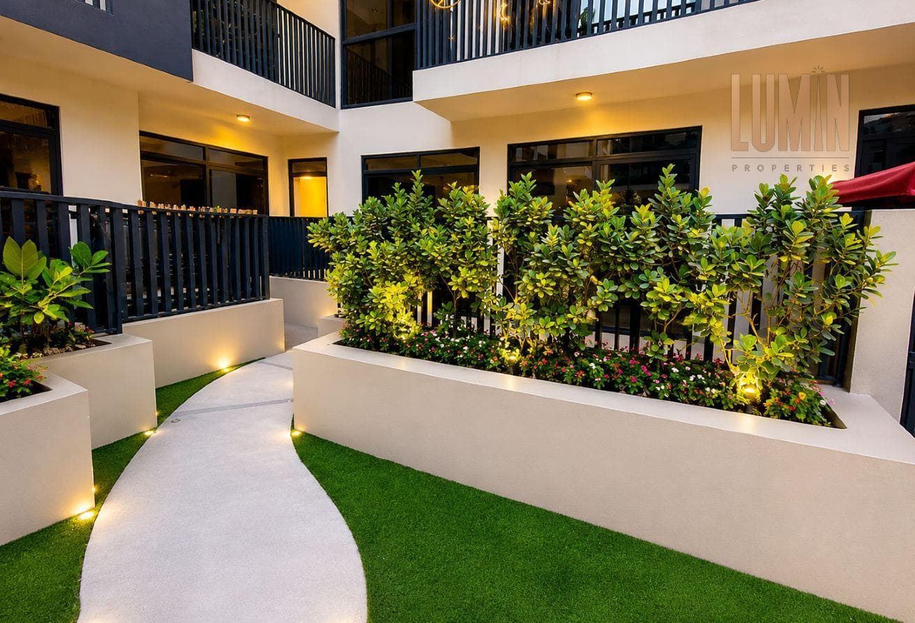 Lit garden path between planters outside ground-floor apartments at Lucky 1 Residence, JVC